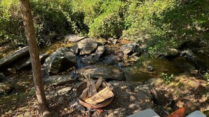 A rustic outdoor seating area with a fire pit and a small stream. - Whispering Waters Dome Getaway (Cosby)
