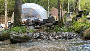 A tented accommodation with a stone wall and a stream in a forested area. - Moonshine Hollow Dome by Rafting (Cosby)