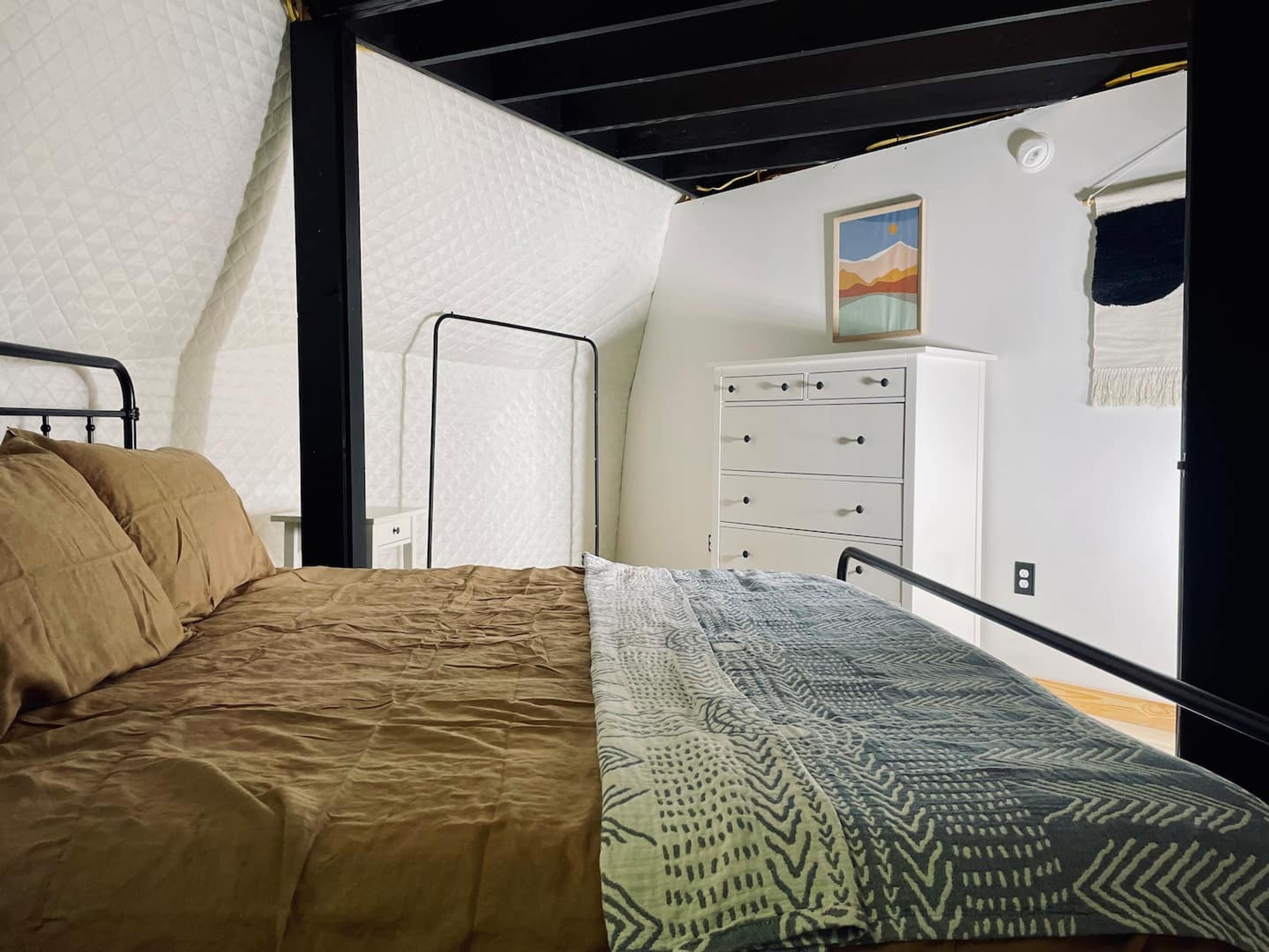 A bedroom with a bed, a dresser, and a painting on the wall.