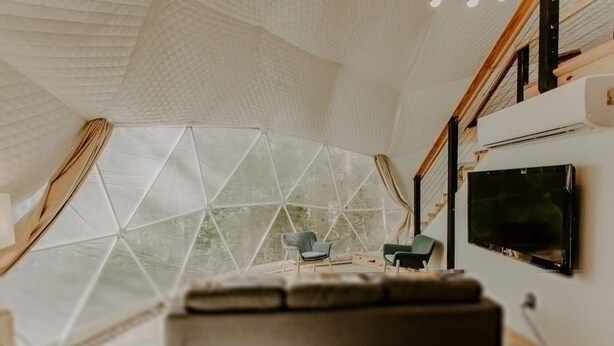 A modern living room with a large geometric glass wall, a flat-screen TV, and a sofa. - Moonshine Hollow Dome by Rafting (Cosby)