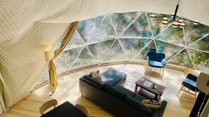 A modern, spacious living area with a large, curved glass wall offering a view of the outdoors. - Moonshine Hollow Dome by Rafting (Cosby)