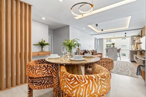 Et moderne spiseområde med et rundt træbord, stole med zebra-mønster og en moderne lampe.