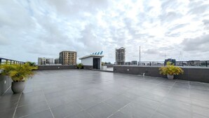 Une terrasse sur le toit, dotée d’un sol carrelé, de plantes en pot et d’un petit bâtiment surmonté d’un toit bleu.