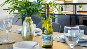 Una mesa de comedor con una botella de vino, un jarrón con flores y copas de vino vacías.