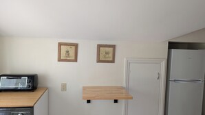A kitchen with a toaster, two framed pictures, a wooden shelf, and a refrigerator. - Sweetgum Hideaway Home (Athens)