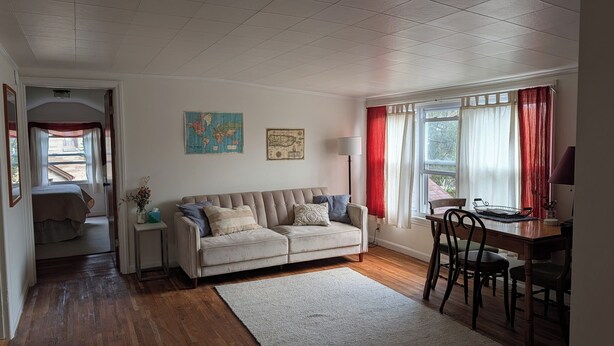 A cozy living room with a sofa, a dining table with chairs, a world map on the wall, and a window with curtains. - Sweetgum Hideaway Home (Athens)