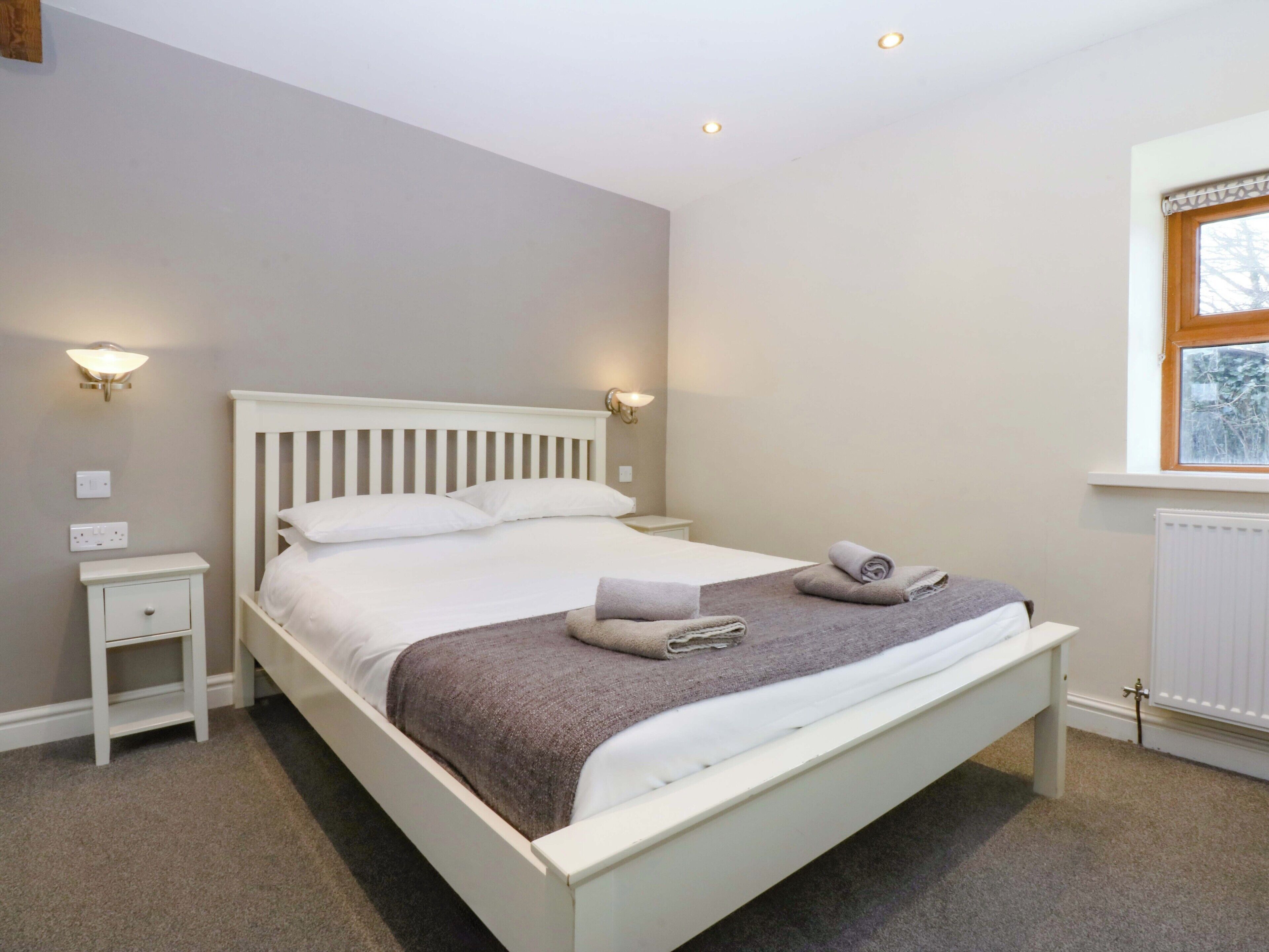 A neatly made bed with pillows and a blanket, two bedside tables, and wall-mounted lights.