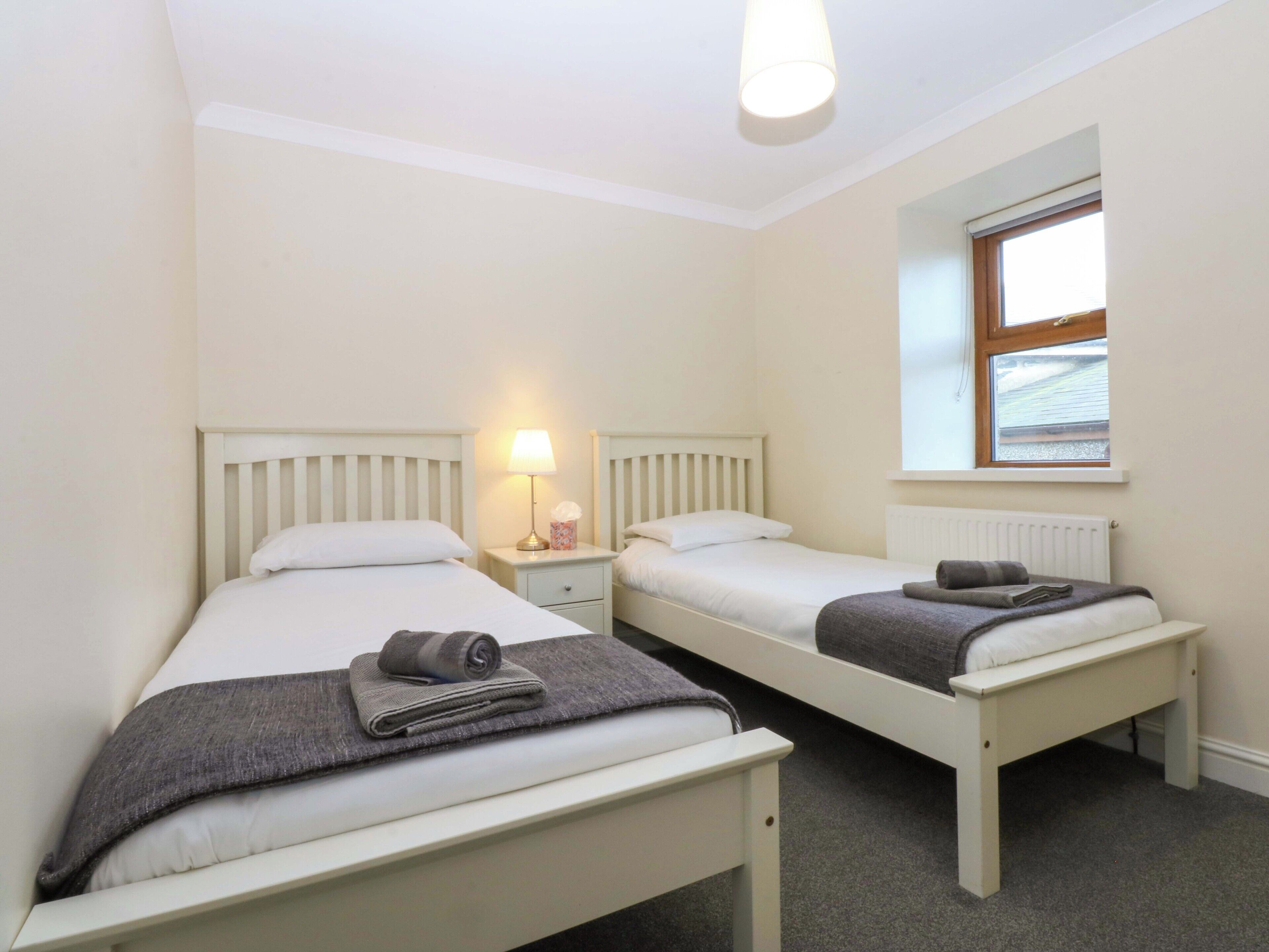 A room with two single beds, a nightstand with a lamp, a window with a view, and a radiator.
