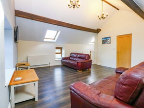 Un vaste salon doté d’un haut plafond, de poutres apparentes, d’un canapé en cuir, d’une table en bois et d’un radiateur.
