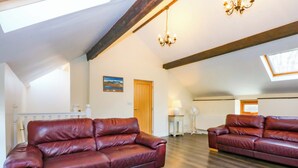 Ein geräumiges Schlafzimmer im Loft-Stil mit geneigten Decken, Holzbalken, einem großen Fenster, zwei Ledersofas, einem Nachttisch, einer Stehlampe und einem Gemälde an der Wand.