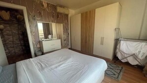 A bedroom with a large bed, a wardrobe, a mirror, and a drying rack.