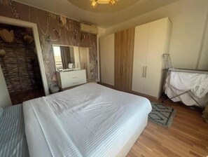 A bedroom with a large bed, a wardrobe, a mirror, and a drying rack.