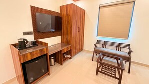 A compact room with a wooden cabinet, a small refrigerator, a bench, and a television mounted on the wall. - Rasa Boutique Stay (Greater Noida)