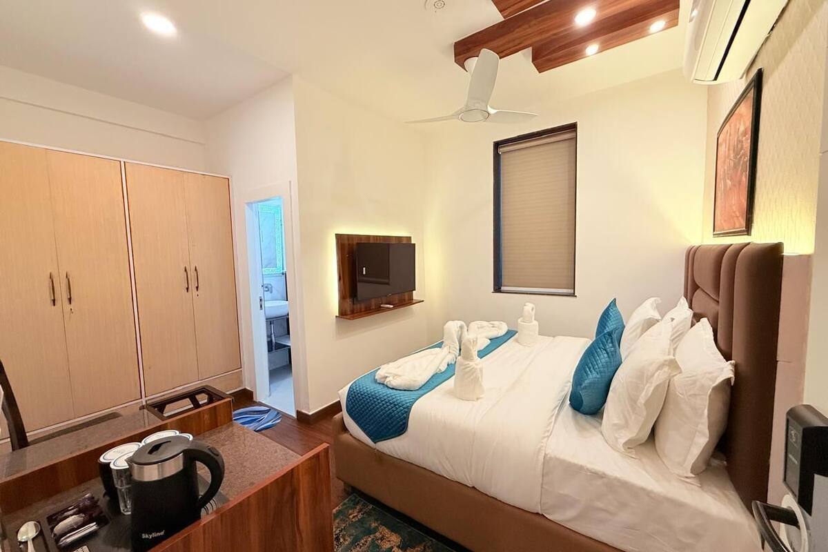 Una camera d'albergo con un letto, una scrivania con bollitore, televisione e armadio.