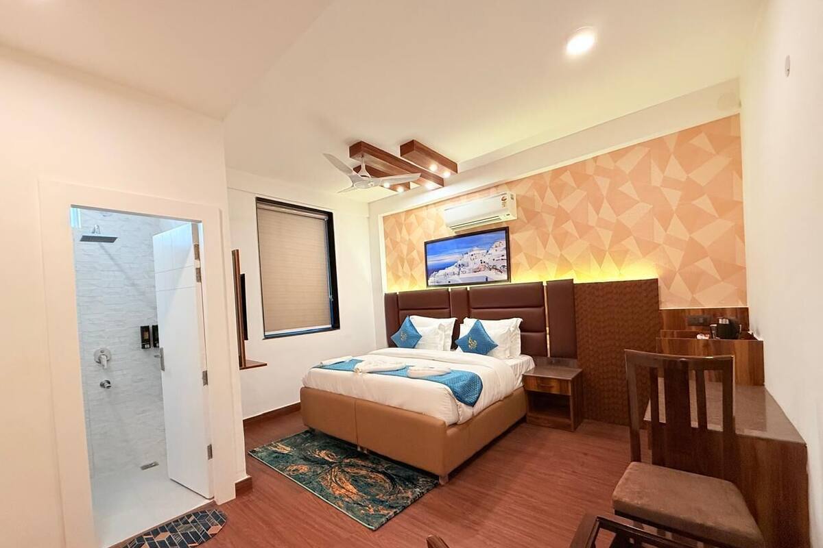 Una camera d'albergo con un letto, una scrivania, una sedia, una televisione e un angolo doccia.