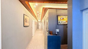A hotel hallway with wooden ceiling beams, a reception desk, and framed pictures on the walls. - Rasa Boutique Stay (Greater Noida)