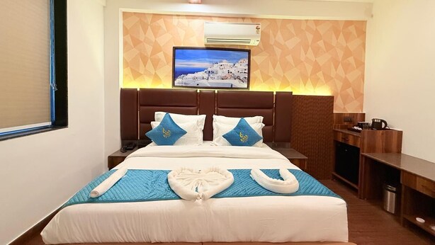 A hotel room with a bed, a TV mounted on the wall, a desk, and a small kitchenette. - Rasa Boutique Stay (Greater Noida)