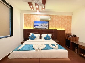 Ein Hotelzimmer mit einem Bett, einem an der Wand montierten Fernseher, einem Schreibtisch und einer kleinen Küchenzeile.