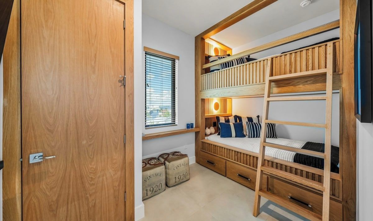 Una habitación con una cama individual superpuesta, un armario de madera y una ventana con persianas.