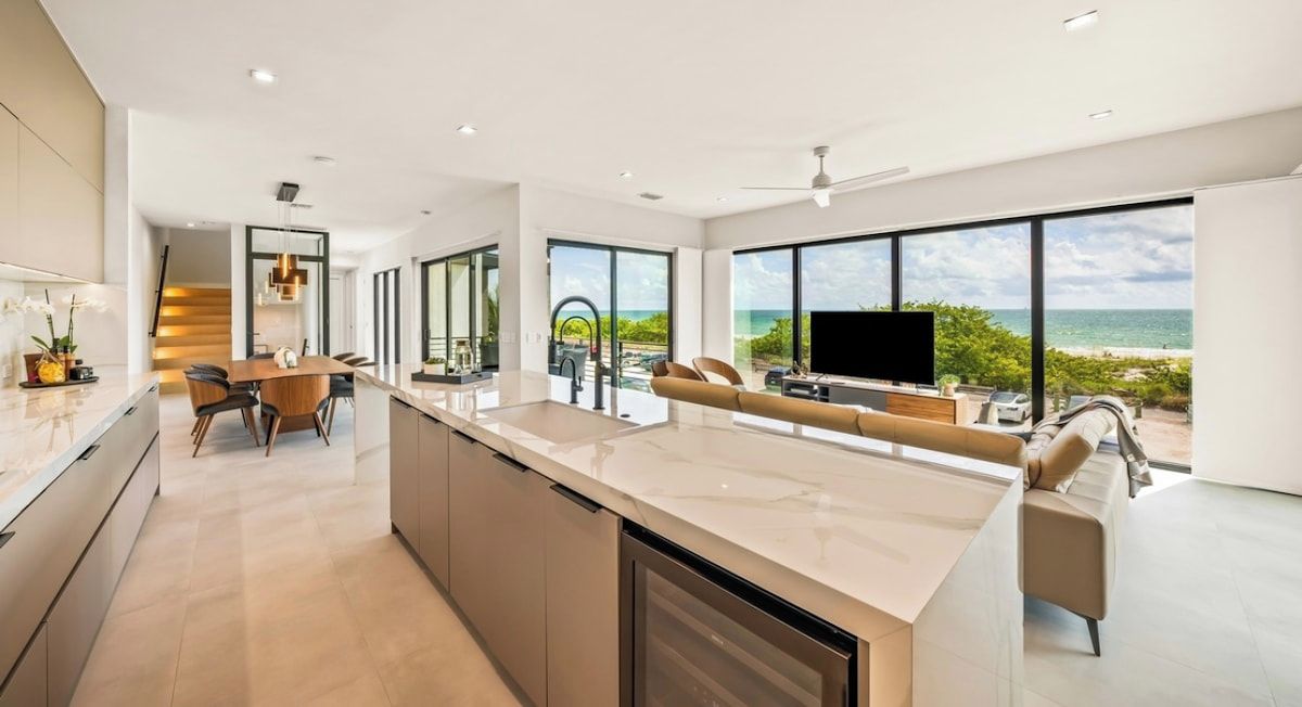 A modern kitchen with a central island, a dining area with a table and chairs, and a living area with a sofa and TV.
