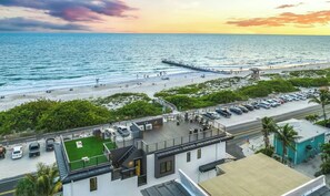 A coastal hotel with a parking area, a beach view, and a pier extending into the water.