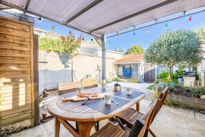 Eine Terrasse im Freien mit einem runden Holztisch, Stühlen und einem überdachten Bereich.