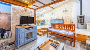 A cozy living area with a TV, wooden furniture, stone walls, and a kitchen.