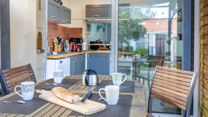 An outdoor dining area with a table, chairs, and a view of the kitchen and garden.
