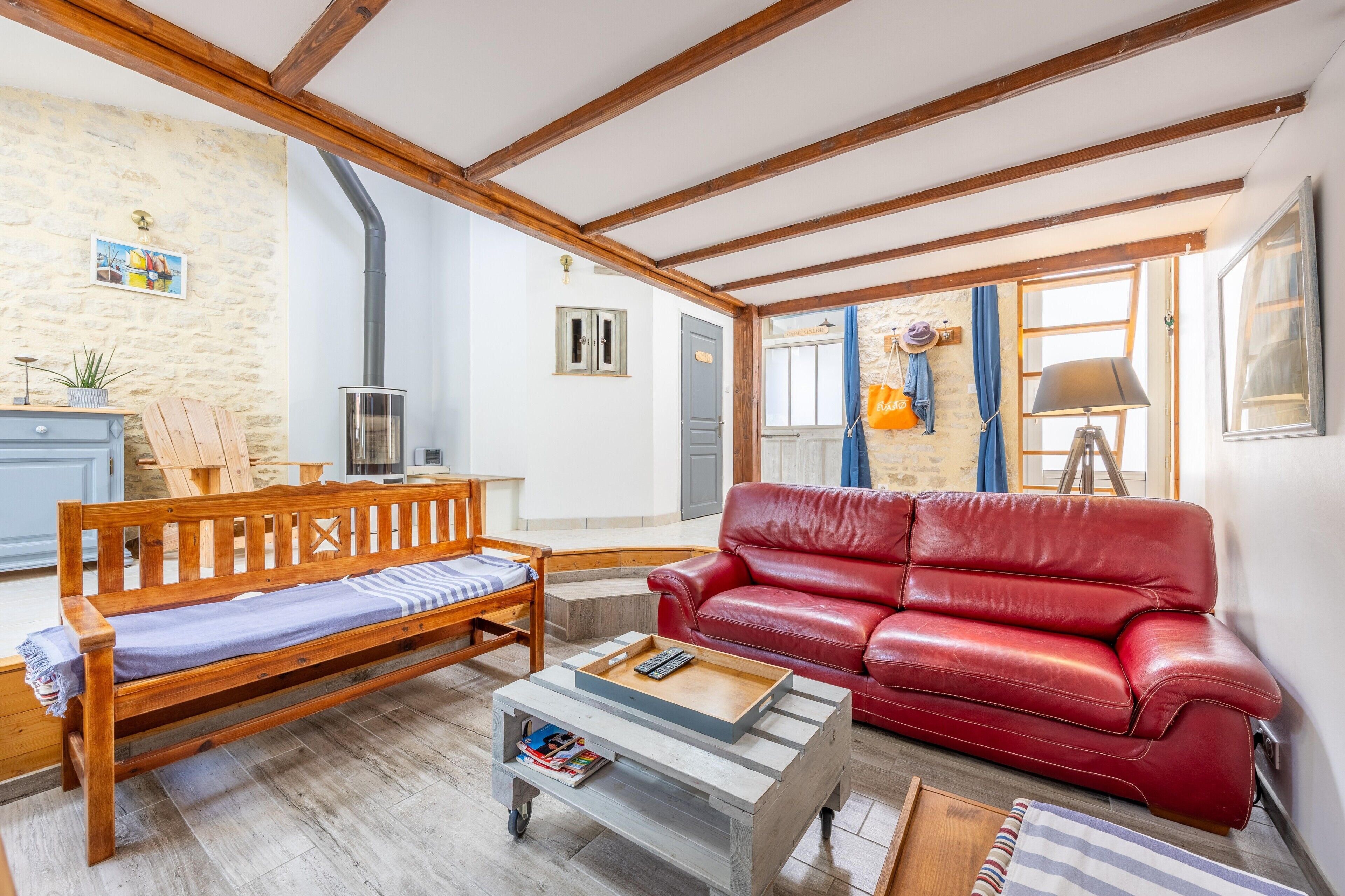 Un salon avec un banc en bois, un canapé en cuir rouge, une table basse et un téléviseur.