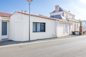 A two-story building with a white facade, a tiled roof, and a visible window with blinds.