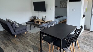 A modern living room with a sofa, a dining table with chairs, a flat-screen TV mounted on the wall, and recessed ceiling lighting. - Getaway 2 steps from the Loire - Loft Ligérien (Sandillon)