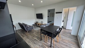 A modern living room with a sofa, a dining table, and a TV mounted on the wall. - Getaway 2 steps from the Loire - Loft Ligérien (Sandillon)
