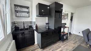 A modern kitchen with black cabinetry, a built-in microwave, and a coffee machine. There is a small dining area with a chair and a table. - Getaway 2 steps from the Loire - Loft Ligérien (Sandillon)