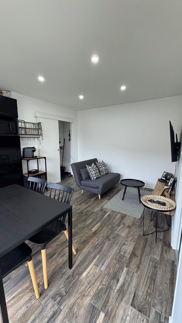Un salon moderne avec un canapé gris, une table à manger et un téléviseur fixé au mur.