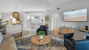 A modern living room with a sofa, a coffee table, and a TV. There is a kitchen in the background. - Oceanwalk 9-302 (New Smyrna Beach)