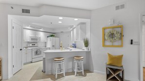 A modern kitchen with white cabinets, a central island with stools, and a yellow accent wall. - Oceanwalk 9-302 (New Smyrna Beach)