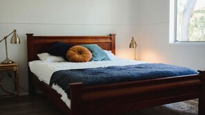 A wooden bed with a white and blue blanket, two bedside lamps, and a window with a view of trees.
