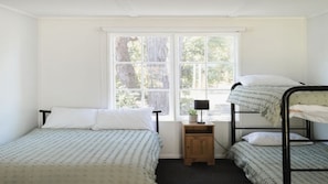 Ein Schlafraum mit zwei Etagenbetten, einem kleinen Nachttisch mit Lampe und einem Fenster mit Blick auf Bäume.