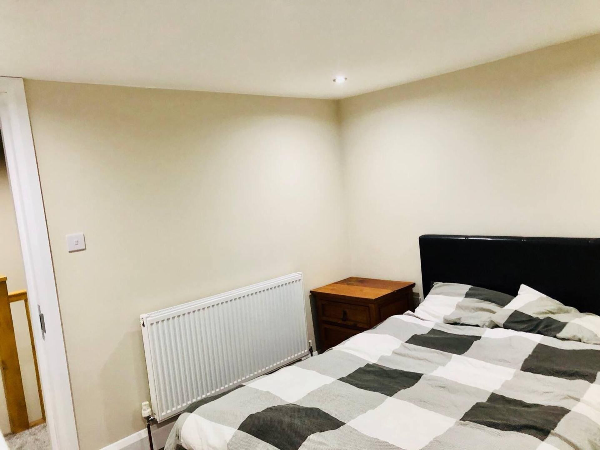 Een slaapkamer met een bed, nachtkastje, radiator en deur.