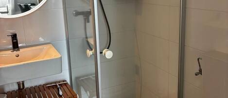 A bathroom with a glass-enclosed shower, a round mirror, a wooden vanity, and a toilet.