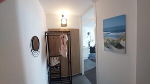 A hallway with a coat rack, a towel rack, a wooden door, and a framed picture of a beach.
