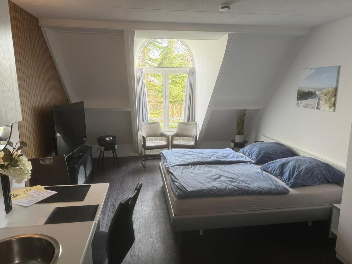 A room with a bed, desk, chair, TV, and a window with curtains.