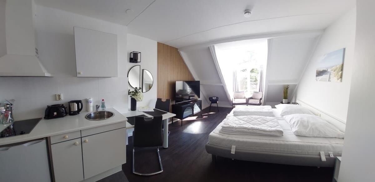 A modern hotel room with a kitchenette, a bed, a desk, and a large window.