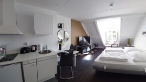 A modern hotel room with a kitchenette, a bed, a desk, and a large window.