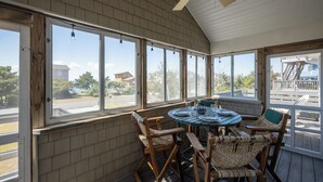 Une terrasse couverte avec une table ronde et des chaises en osier, de grandes fenêtres et une vue sur la rue.