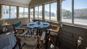 Une terrasse ensoleillée avec une table ronde dressée pour le repas, entourée de chaises en osier, et de grandes fenêtres offrant une vue sur le quartier.