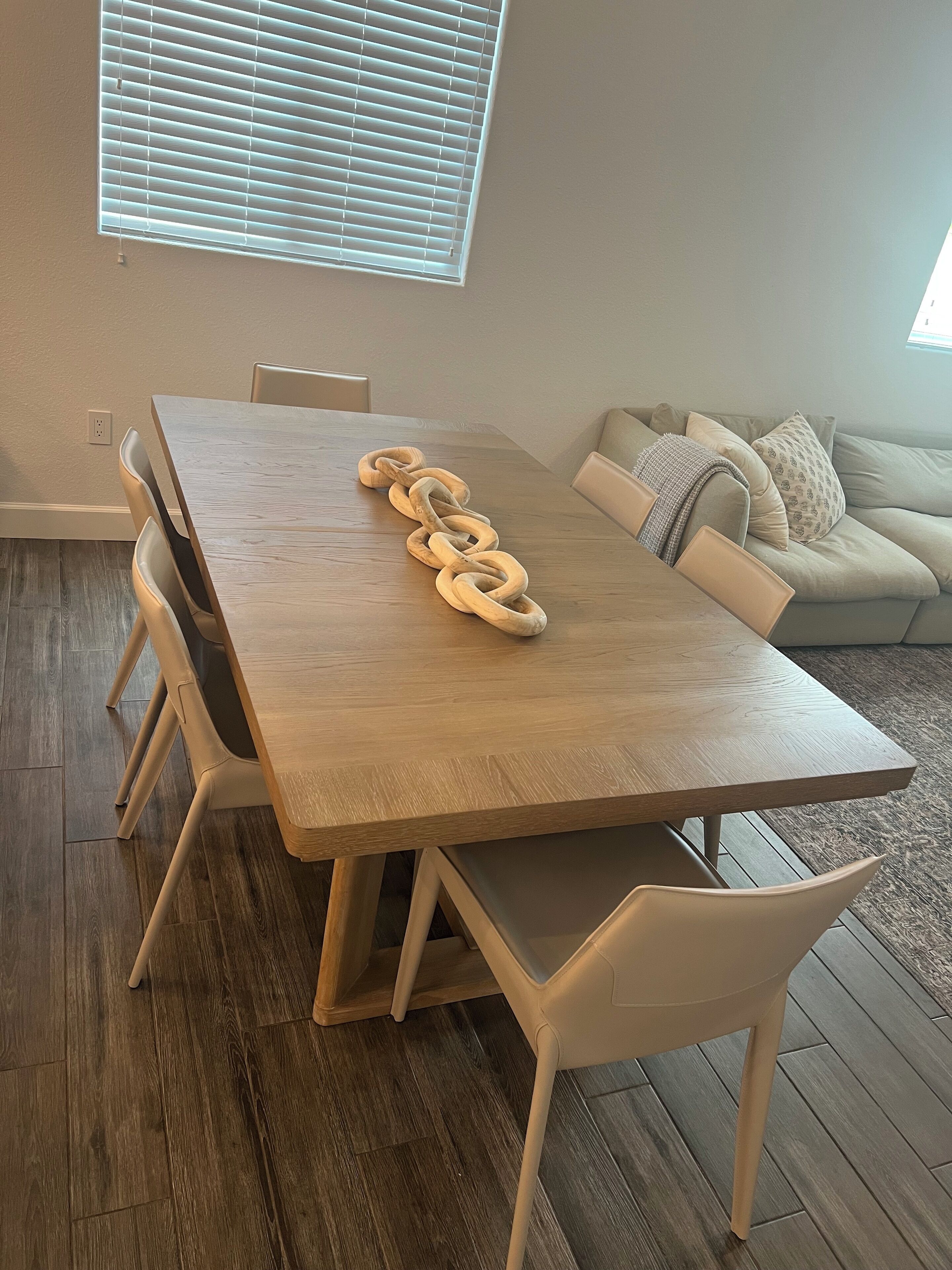 A dining area with a wooden table, white chairs, and a wooden chain centerpiece.