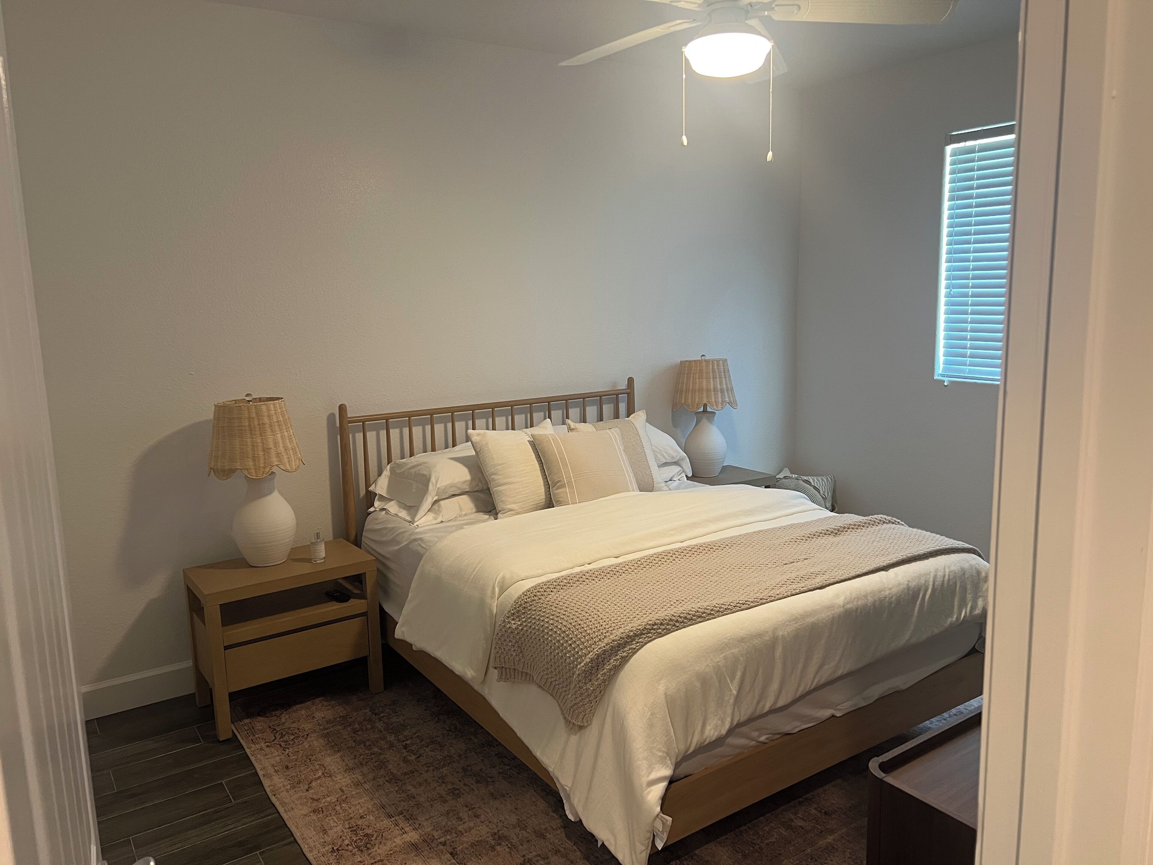 Een slaapkamer met een bed, twee nachtkastjes, een plafondventilator en een raam met jaloezieën.