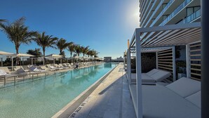 A swimming pool with lounge chairs and umbrellas, surrounded by palm trees and modern buildings. - Luxury View-Modern 1-BR Condo with Panoramic Ocean Views, Pool & Gym–Miami Beach (Miami Beach)