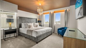 Une chambre d’hôtel moderne avec un grand lit, un bureau avec une lampe, une chaise bleue et une vue sur l’extérieur.